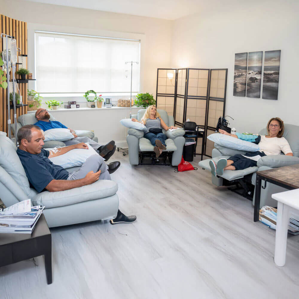 Comfortable infusion lounge with grey recliners, plants, and wall art in a calming, modern space.